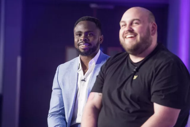 Two male Equans Sci-Tech employees sharing a laugh and talking together during a professional company event, highlighting a friendly and supportive workplace culture